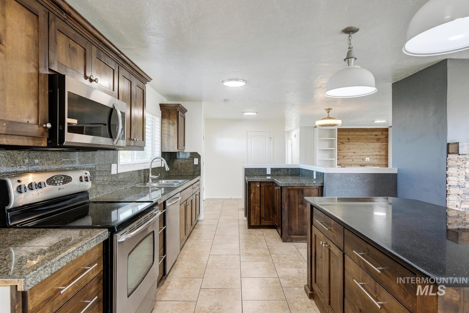 Kitchen featuring stainless steel appliances, a center island, dark brown cabinetry, pendant lighting, and light tile patterned floors