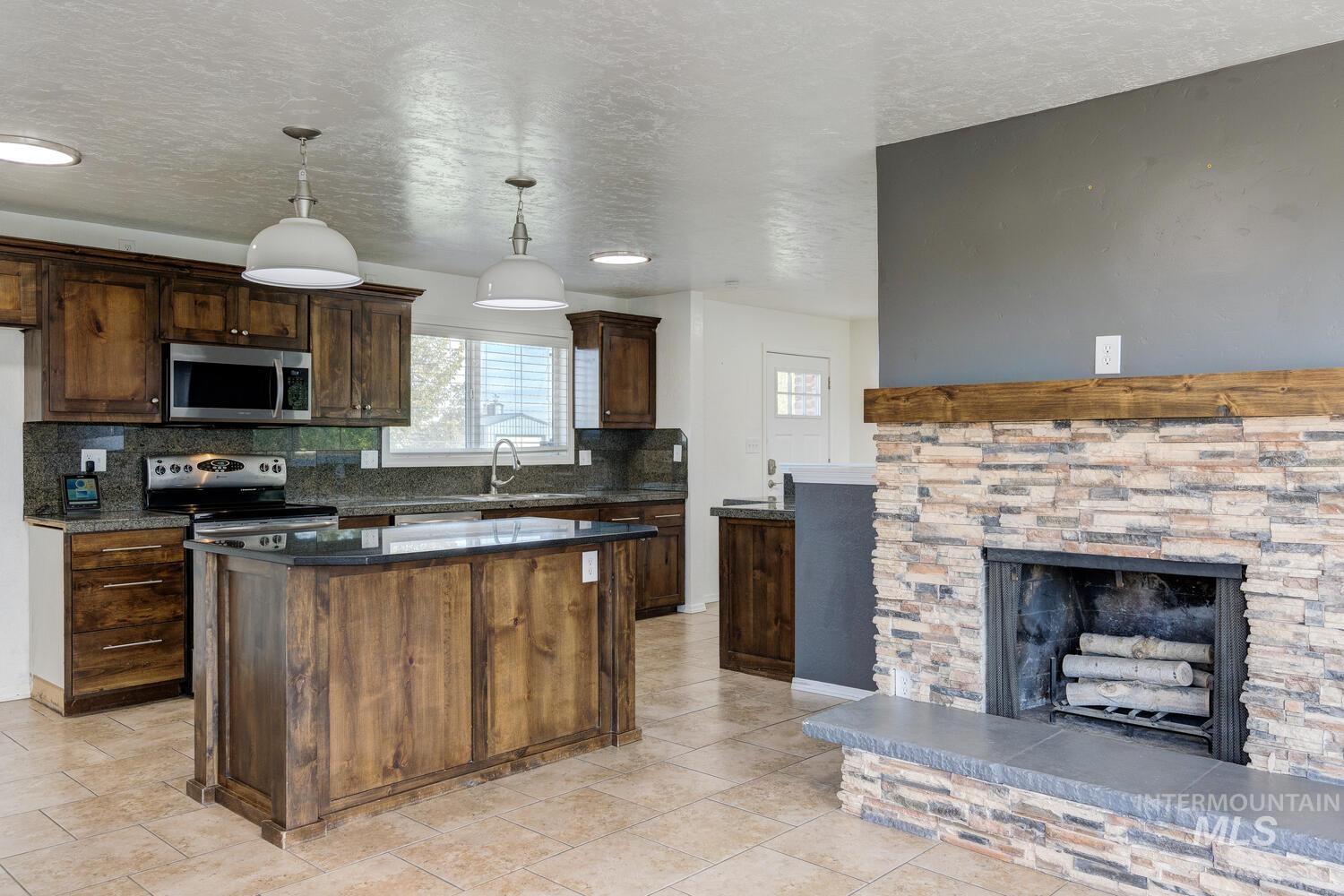 Kitchen featuring dark brown cabinetry, decorative light fixtures, appliances with stainless steel finishes, a textured ceiling, and tasteful backsplash