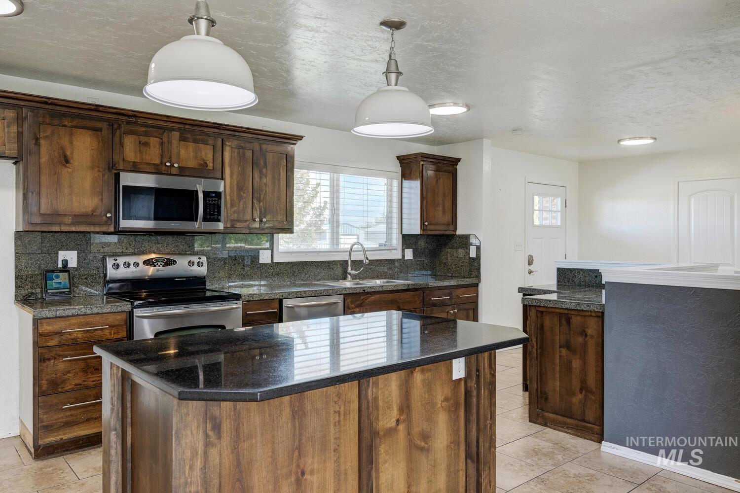 Kitchen featuring appliances with stainless steel finishes, backsplash, a kitchen island, a textured ceiling, and decorative light fixtures