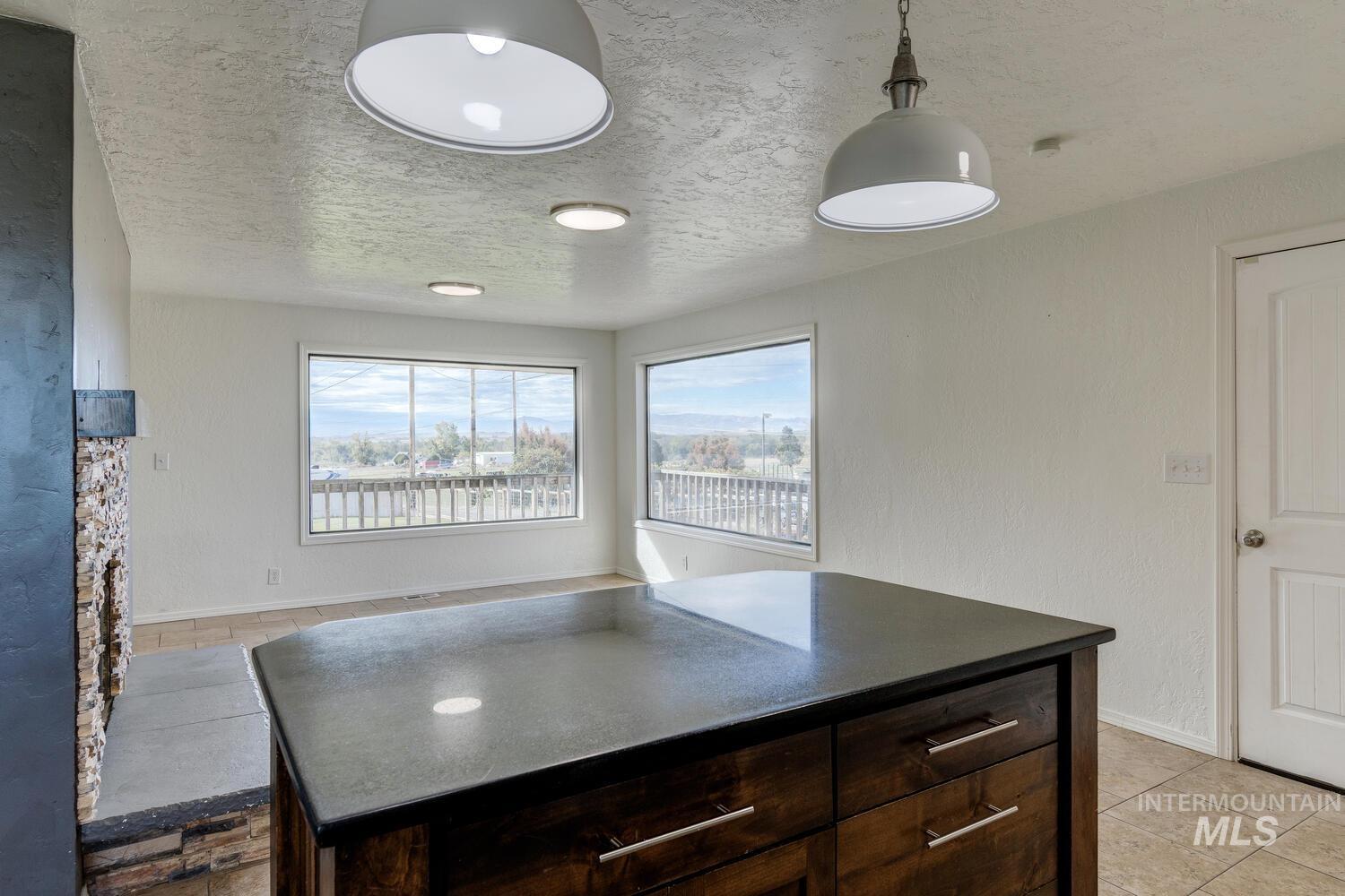 Kitchen featuring dark brown cabinets, a textured ceiling, dark countertops, a kitchen island, and hanging light fixtures