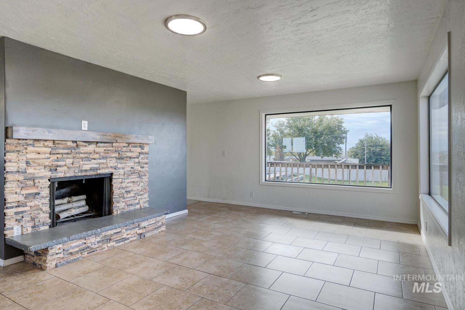 Unfurnished living room featuring a fireplace, a textured ceiling, and light tile patterned flooring