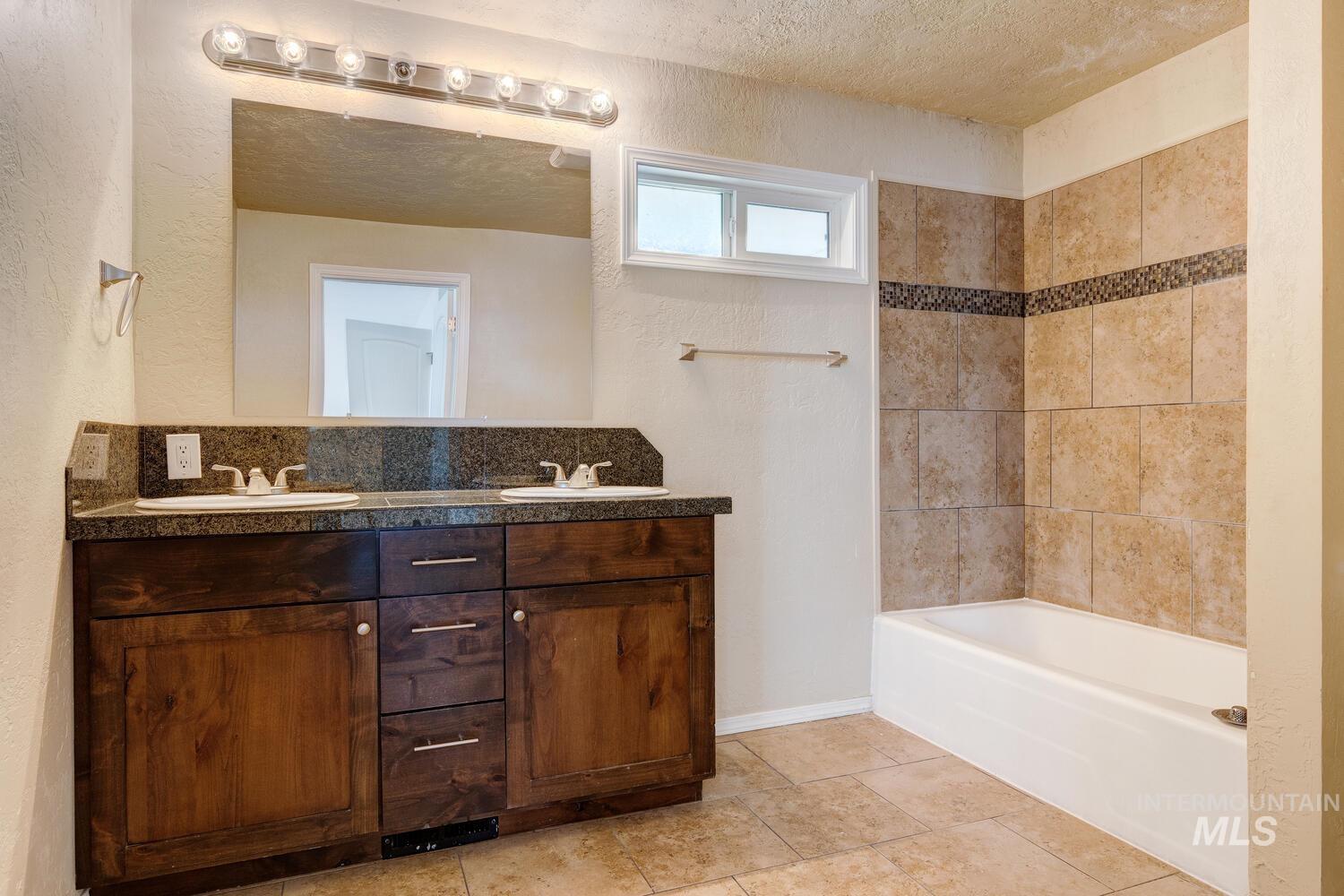 Bathroom with a textured wall, double vanity,  shower combination, and a textured ceiling