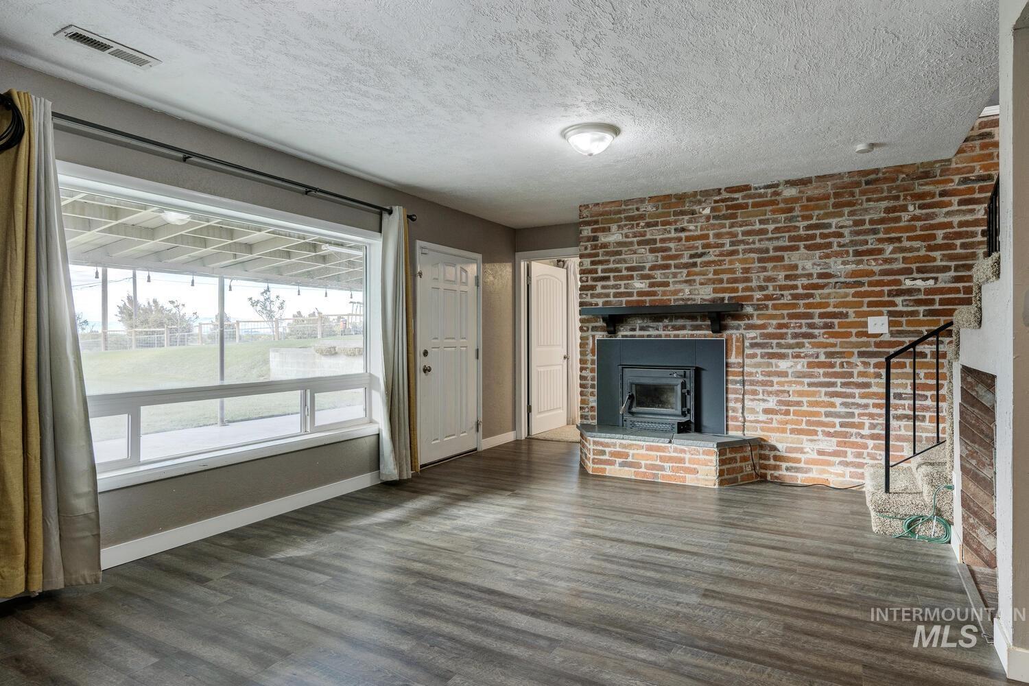 Unfurnished living room with wood finished floors, a textured ceiling, stairway, and brick wall