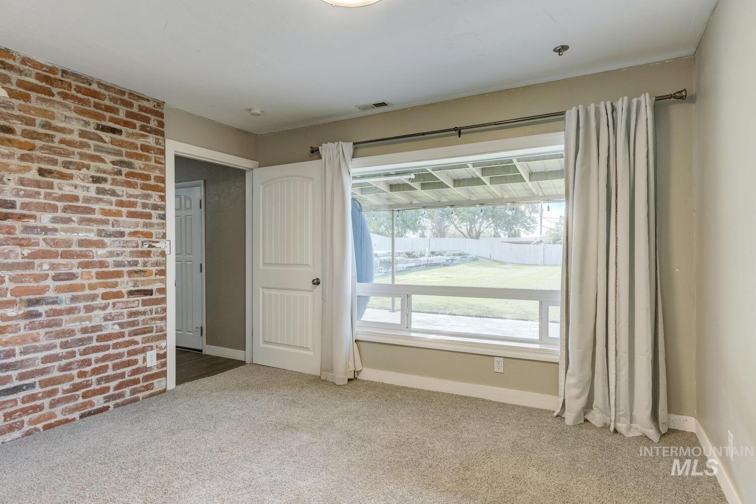 Unfurnished room with light colored carpet and brick wall