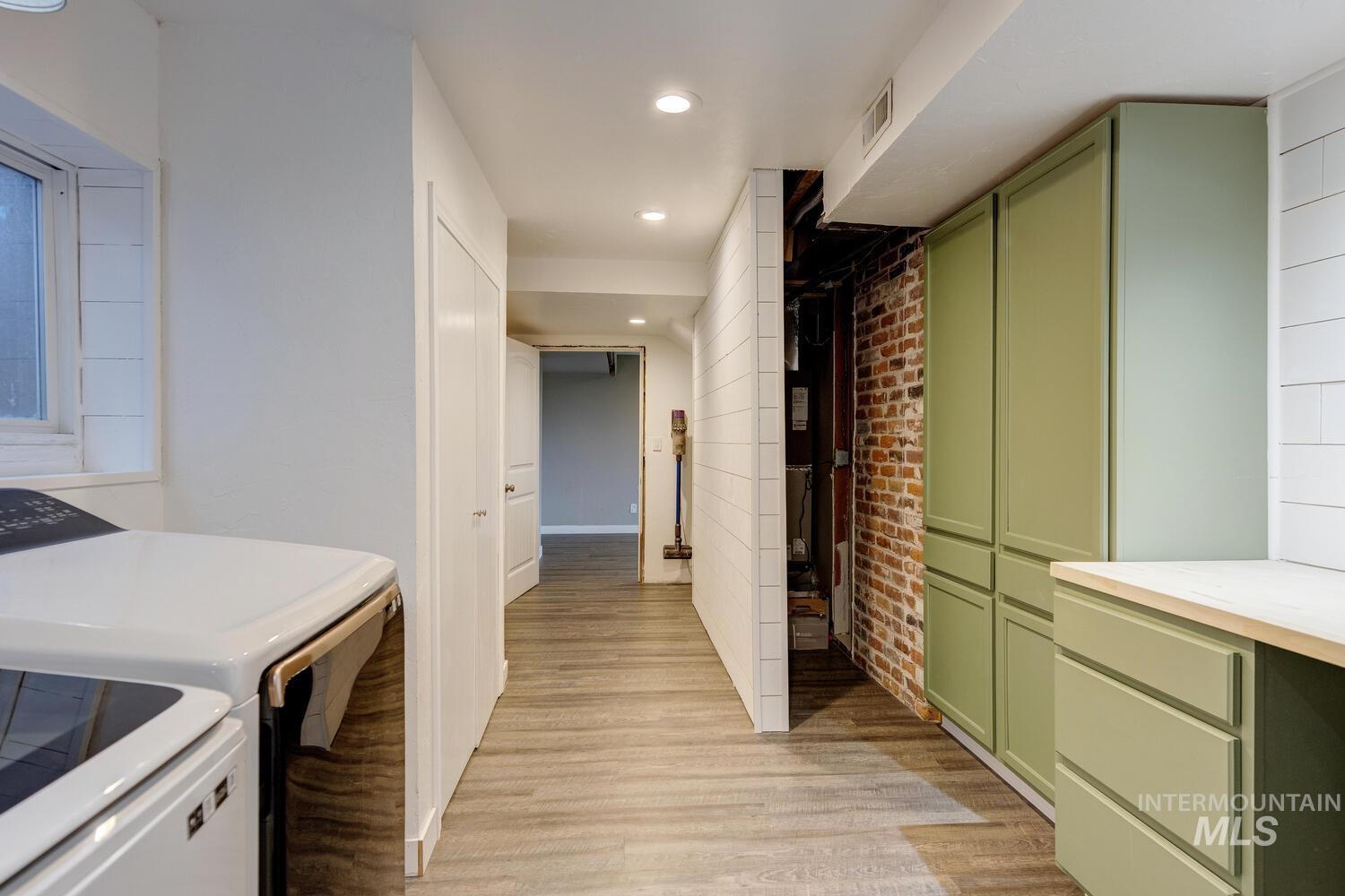 Laundry area with light wood-style floors, recessed lighting, and brick wall