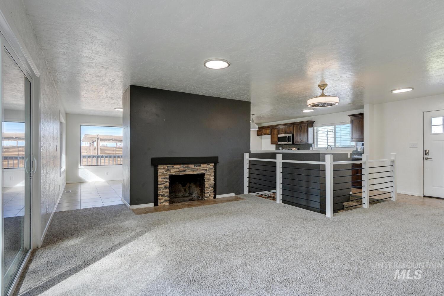 Unfurnished living room featuring light carpet, a fireplace, a textured ceiling, and light tile patterned flooring