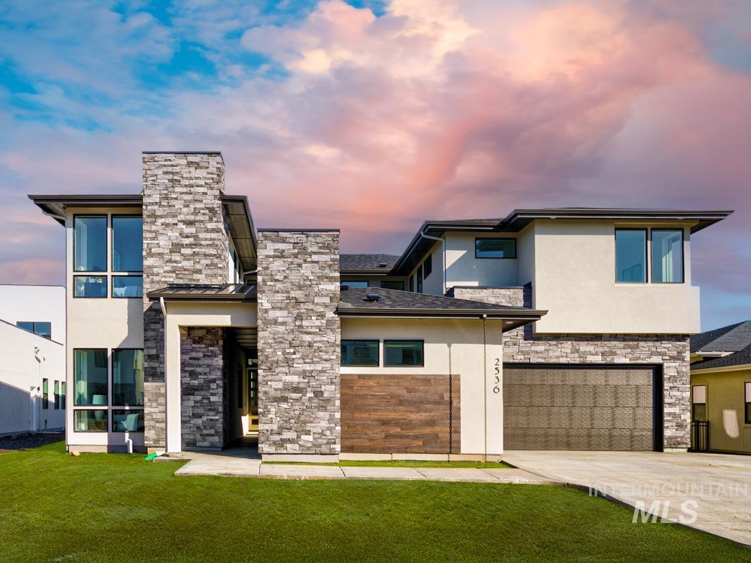 View of front facade with stucco siding, driveway, stone siding, and an attached garage