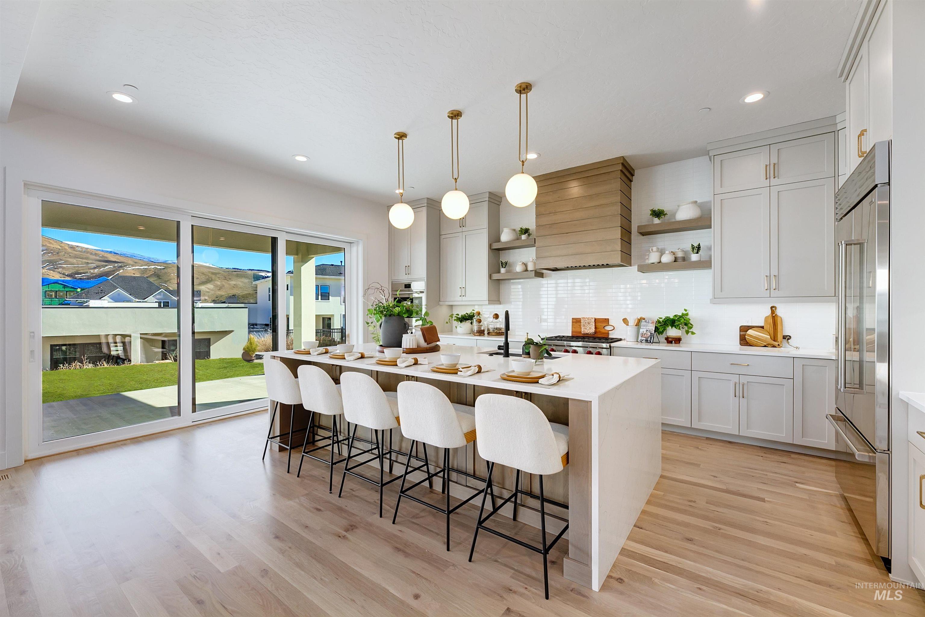 Kitchen featuring decorative light fixtures, light stone countertops, a center island with sink, a breakfast bar area, and open shelves