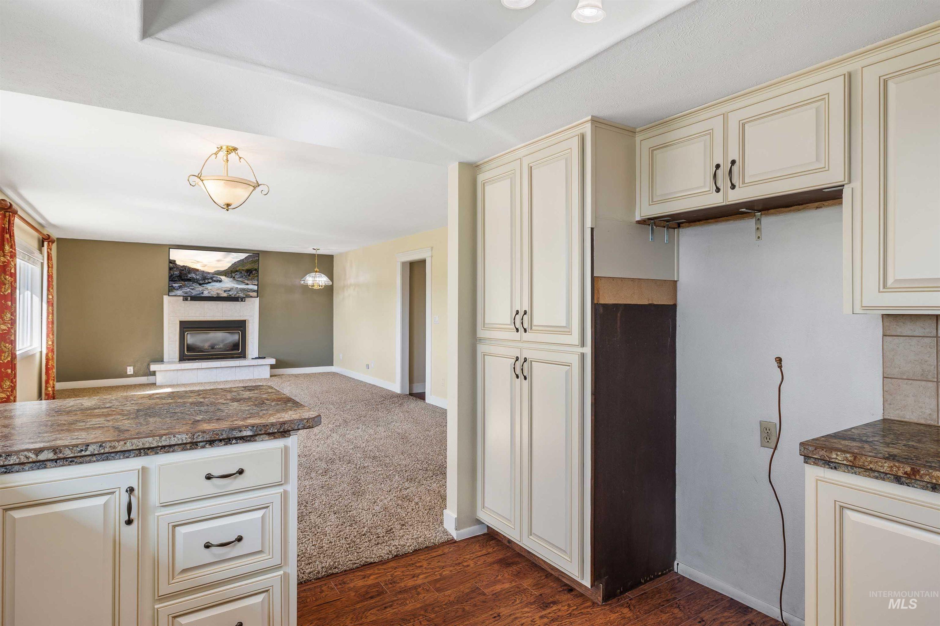 Kitchen featuring cream cabinetry, dark wood finished floors, open floor plan, a glass covered fireplace, and dark carpet