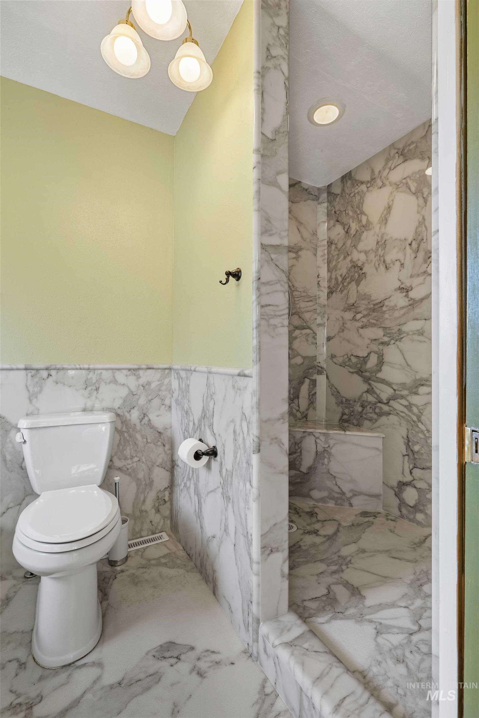 Bathroom featuring tile walls, marble finish floors, a marble finish shower, wainscoting, and recessed lighting