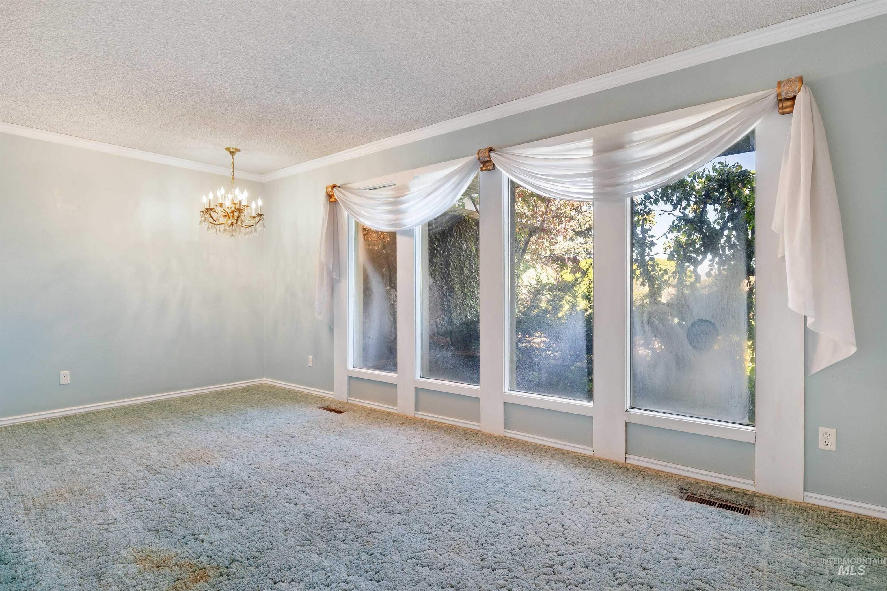 Empty room featuring crown molding, carpet floors, a chandelier, and a textured ceiling