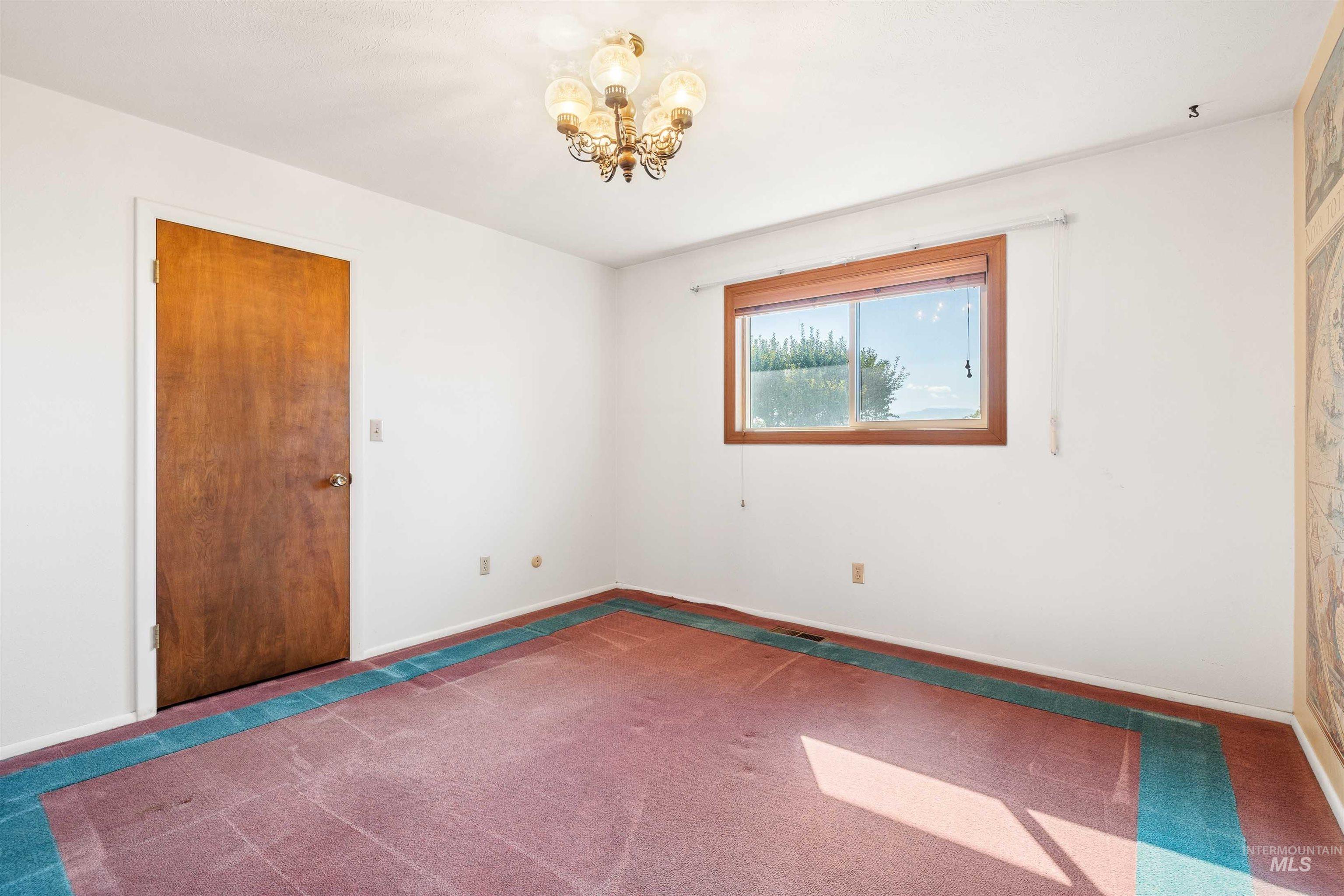Carpeted spare room featuring a chandelier and baseboards