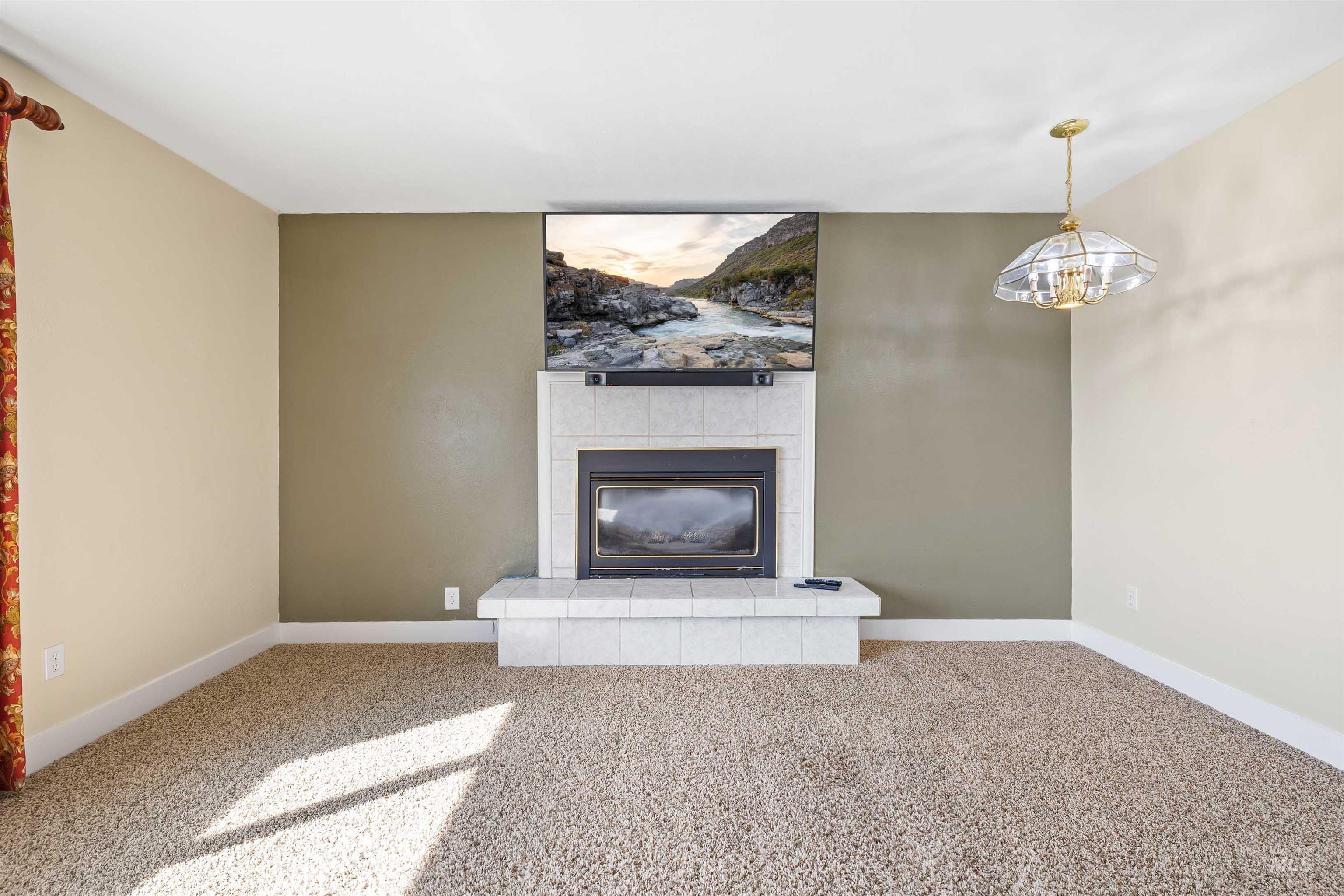 Unfurnished living room with carpet, a tiled fireplace, and a chandelier