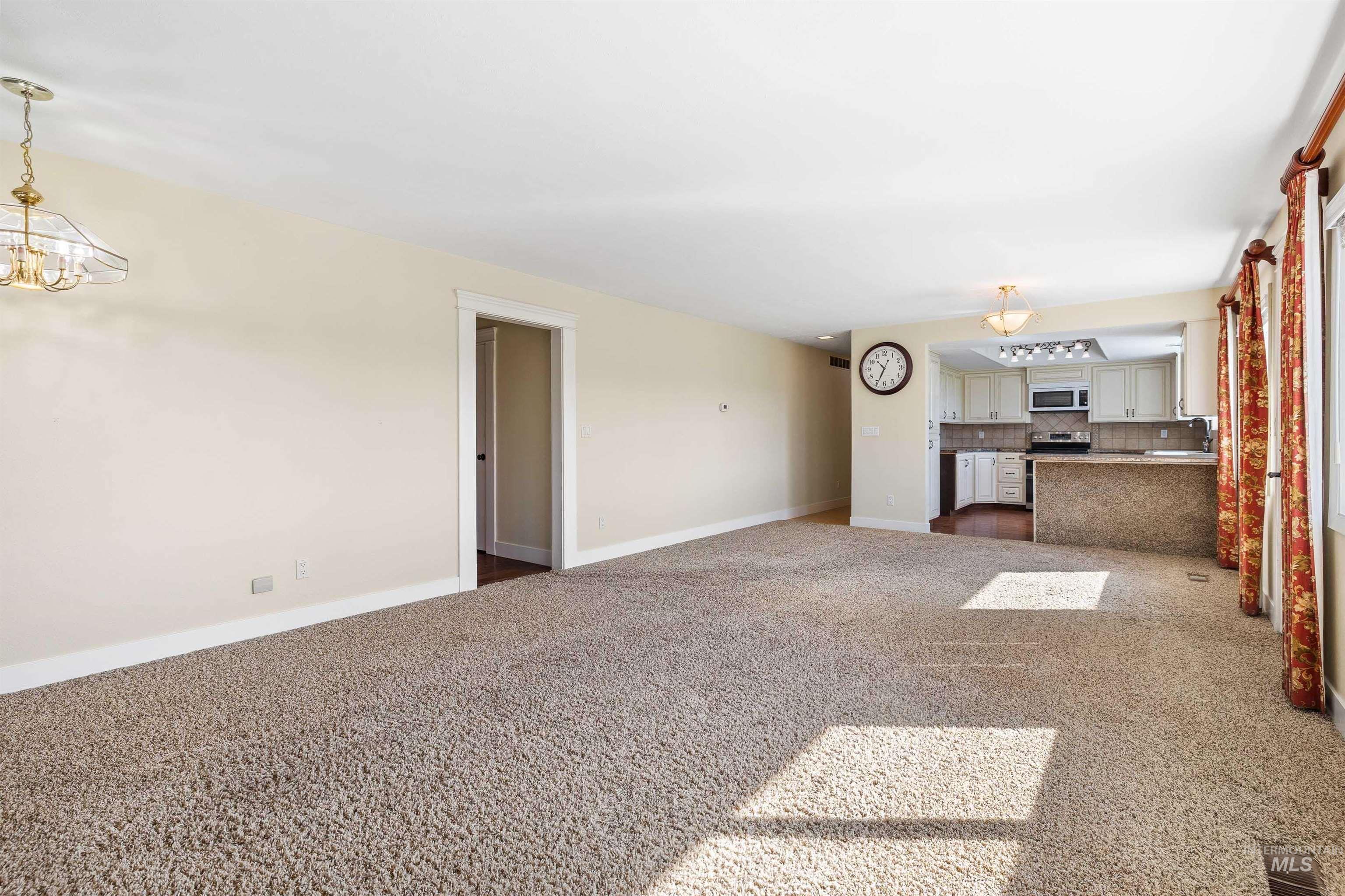 Unfurnished living room featuring dark carpet and a chandelier