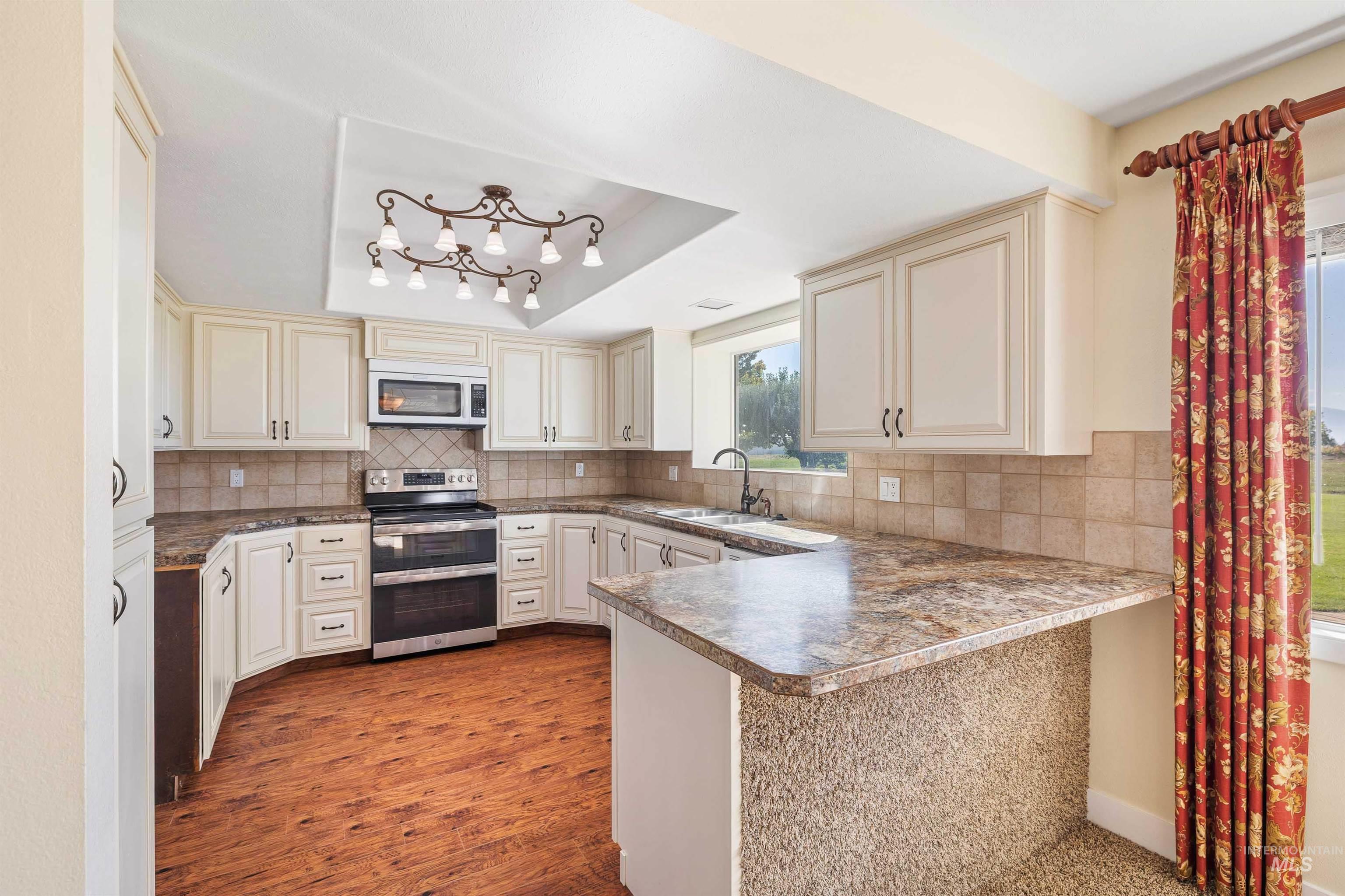 Kitchen with decorative backsplash, a peninsula, a tray ceiling, double oven range, and dark wood finished floors