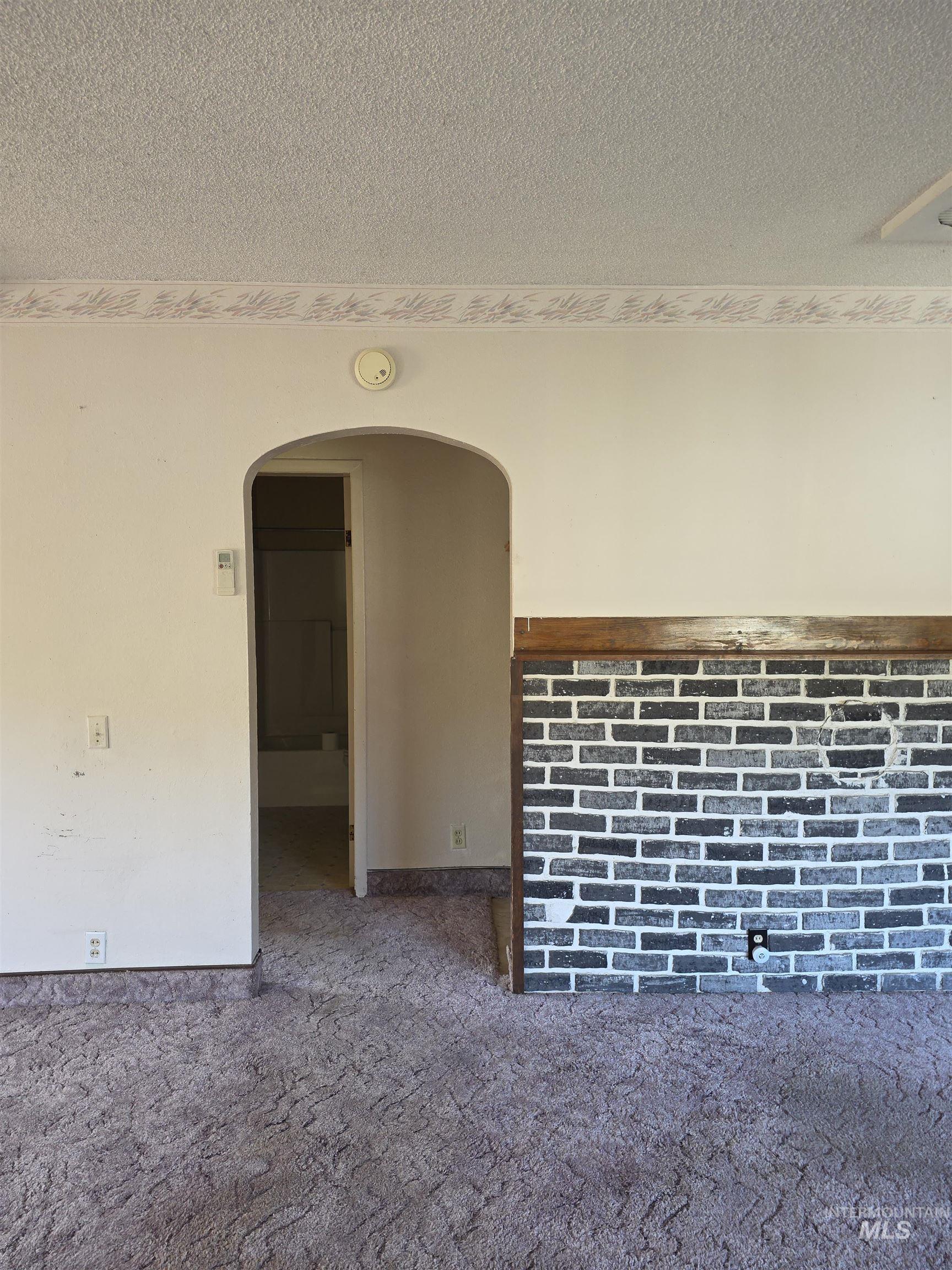 Carpeted spare room with a textured ceiling and arched walkways