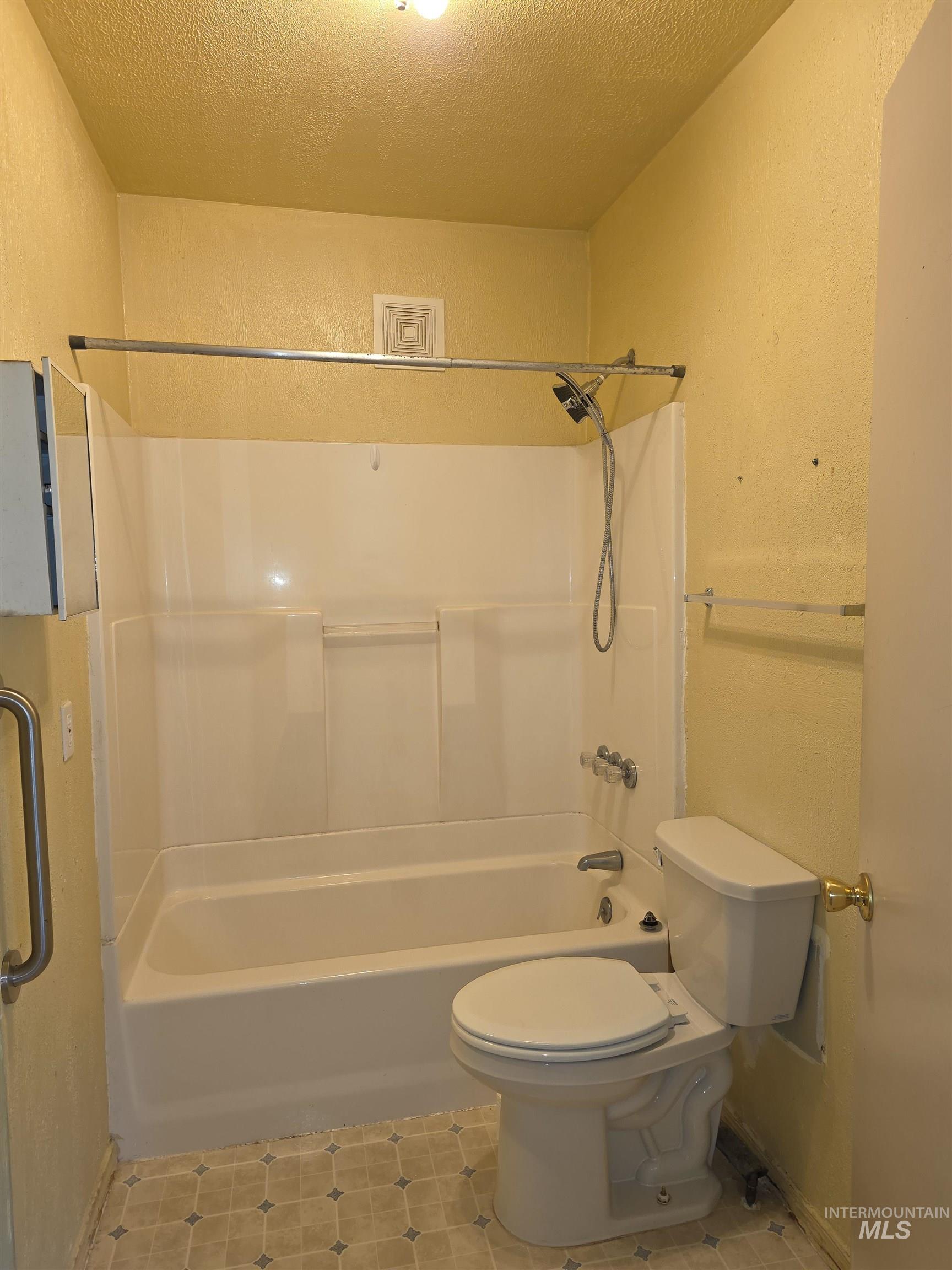 Bathroom with shower / tub combination, a textured wall, a textured ceiling, and light tile patterned flooring