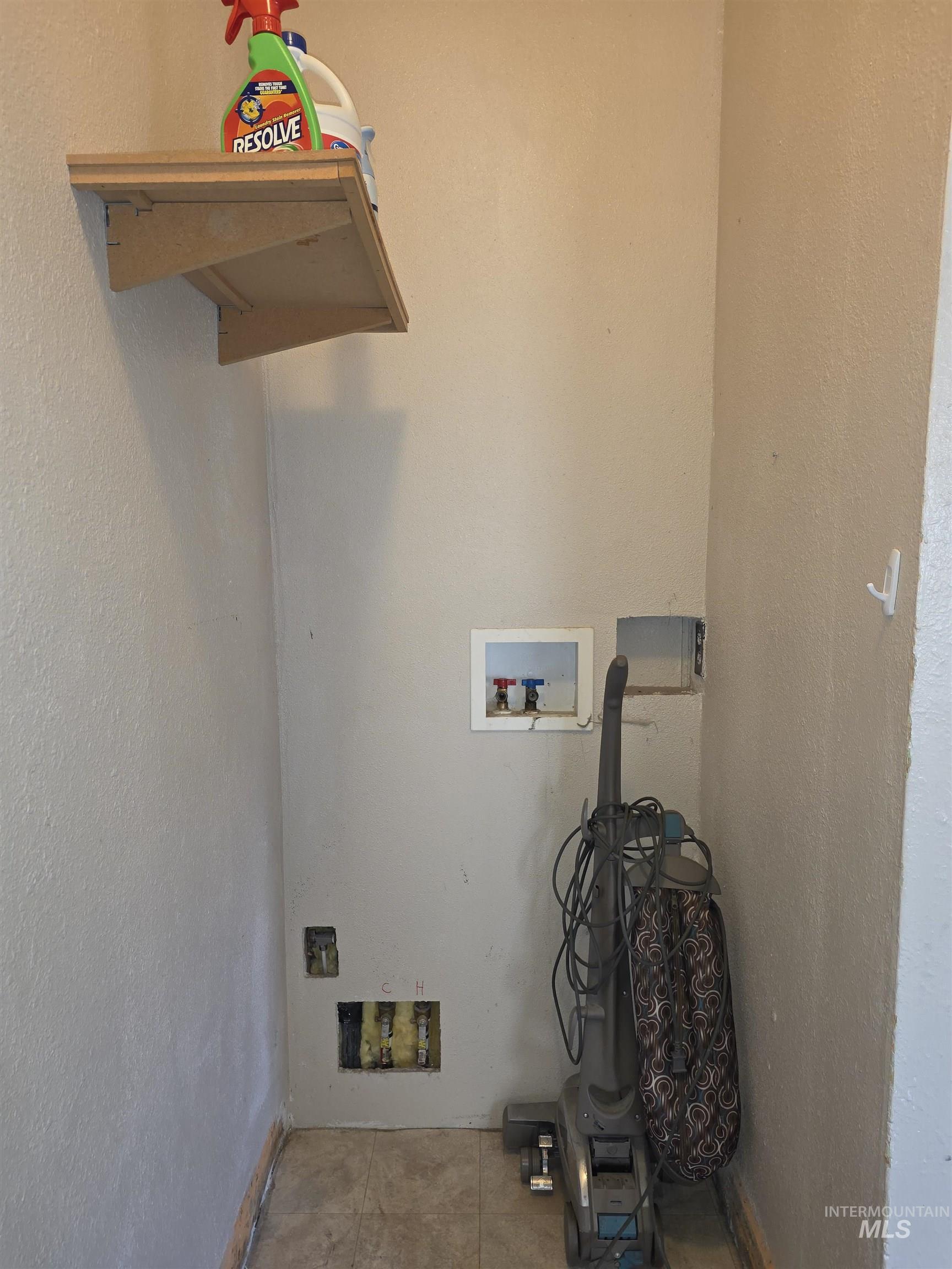 Laundry area with a textured wall, washer hookup, and tile patterned floors