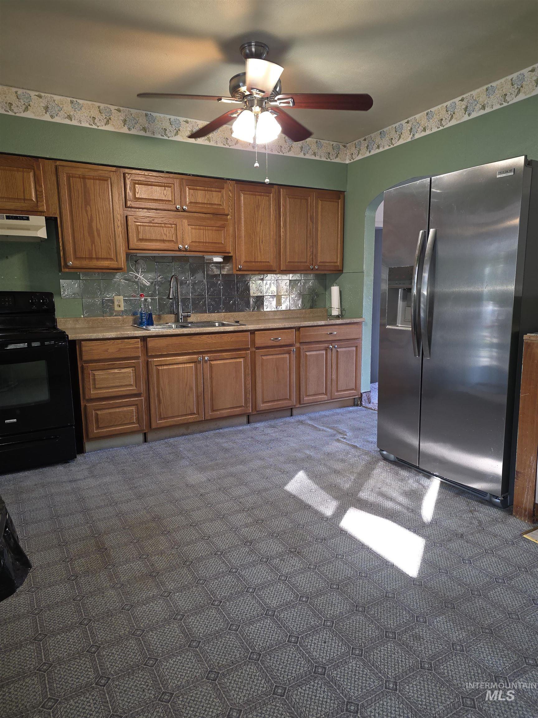 Kitchen featuring stainless steel fridge, tasteful backsplash, black electric range oven, and brown cabinets