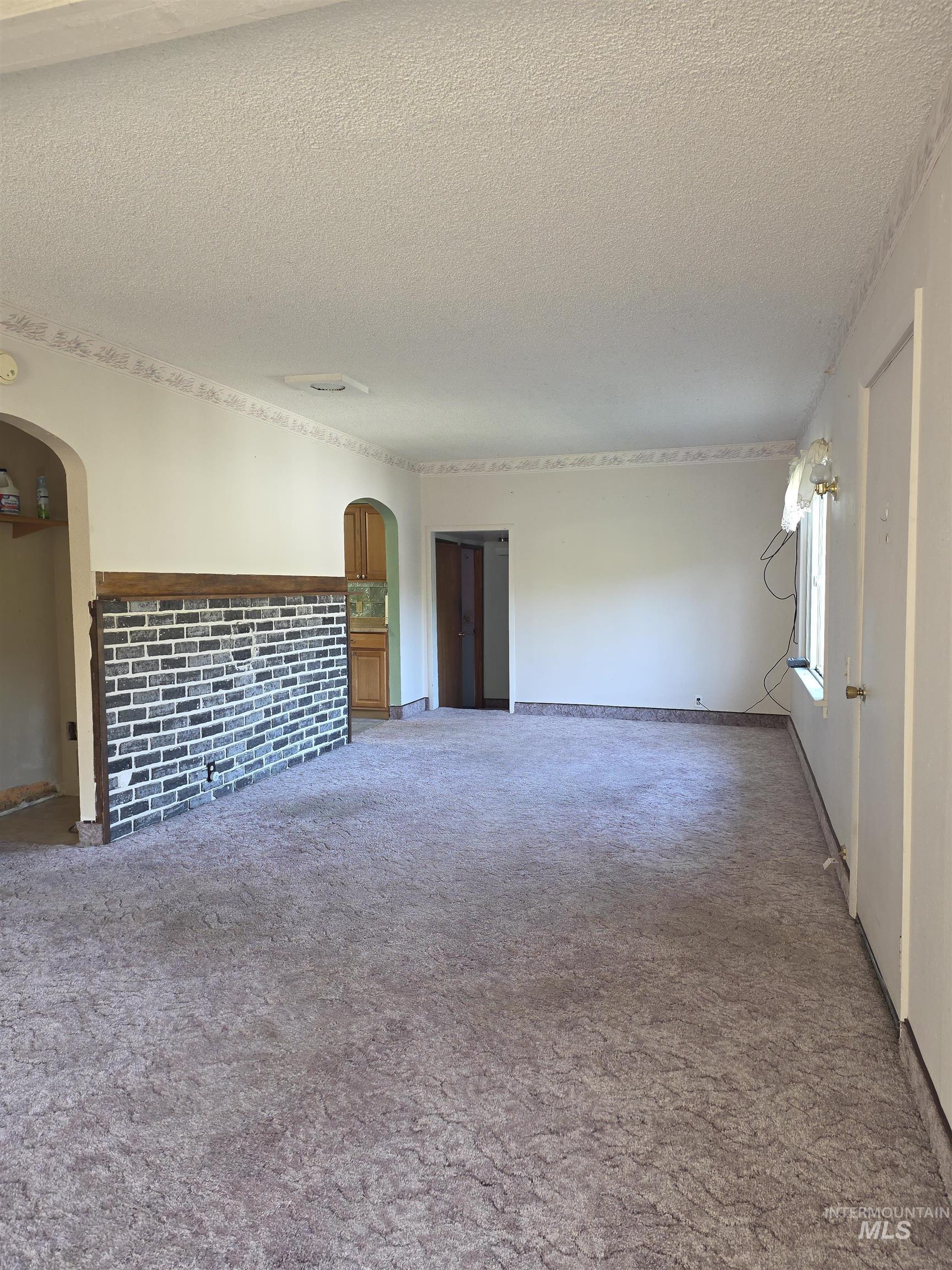 Unfurnished living room featuring arched walkways, carpet flooring, and a textured ceiling