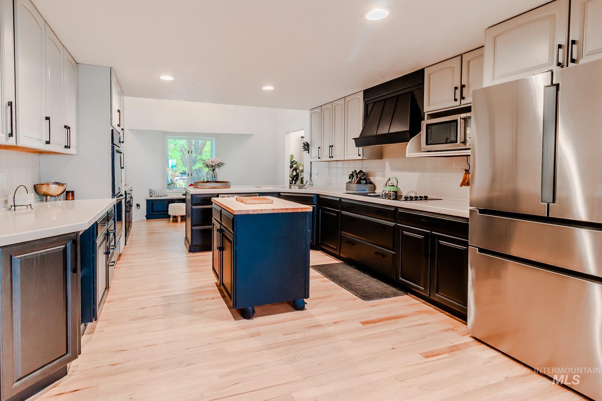 Kitchen with black appliances, premium range hood, butcher block countertops, light wood-style flooring, and recessed lighting