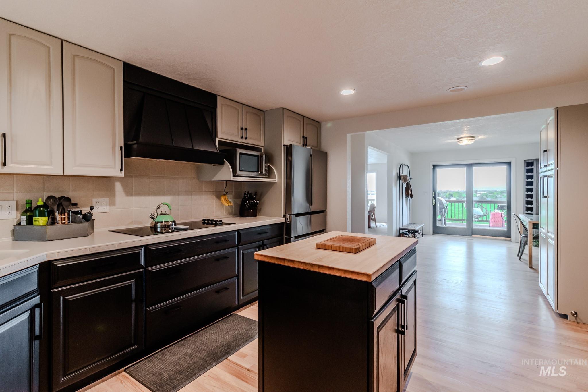 Kitchen featuring appliances with stainless steel finishes, wooden counters, premium range hood, light wood-type flooring, and backsplash