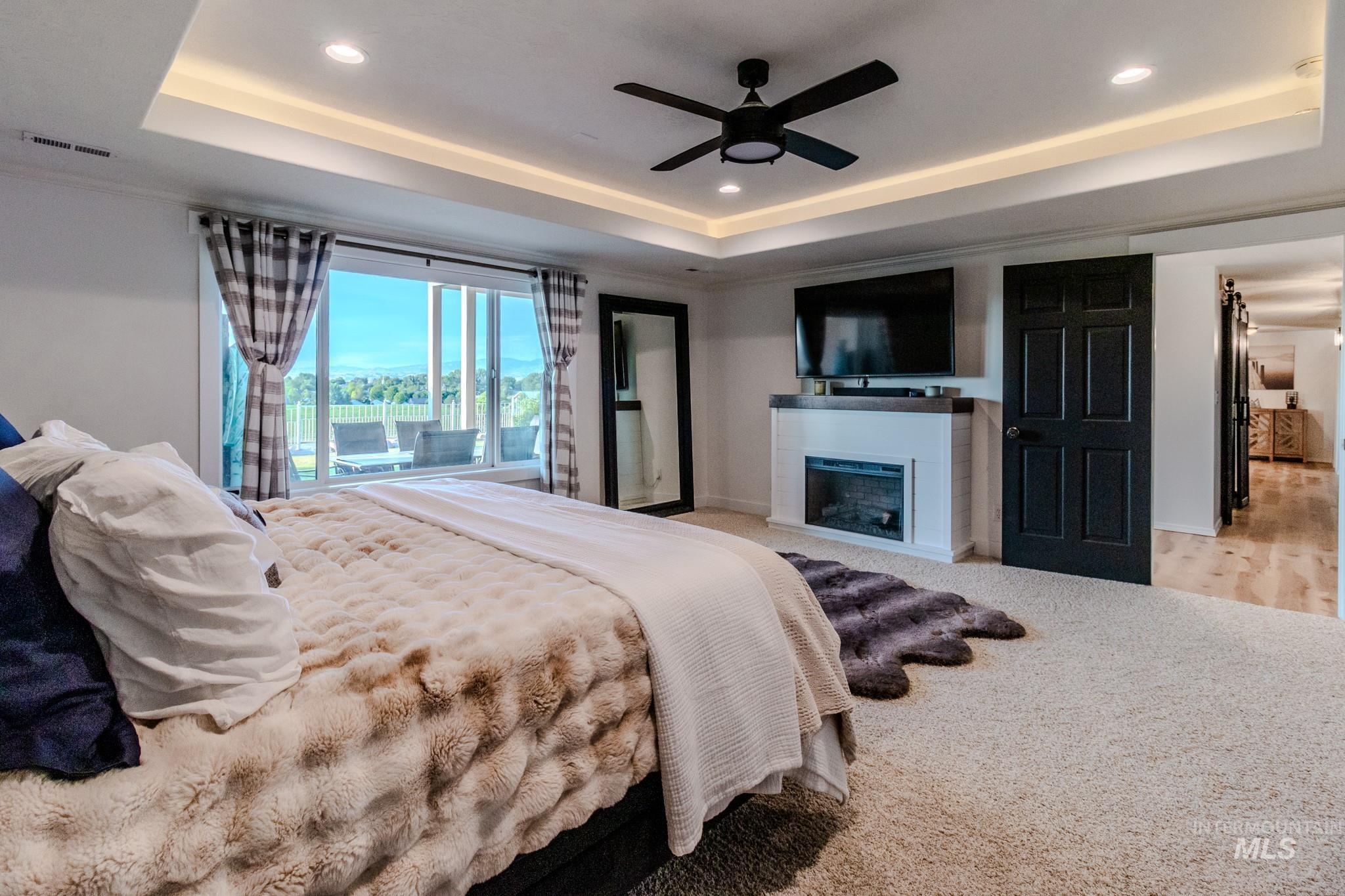 Carpeted bedroom with a tray ceiling, recessed lighting, a fireplace, and ceiling fan