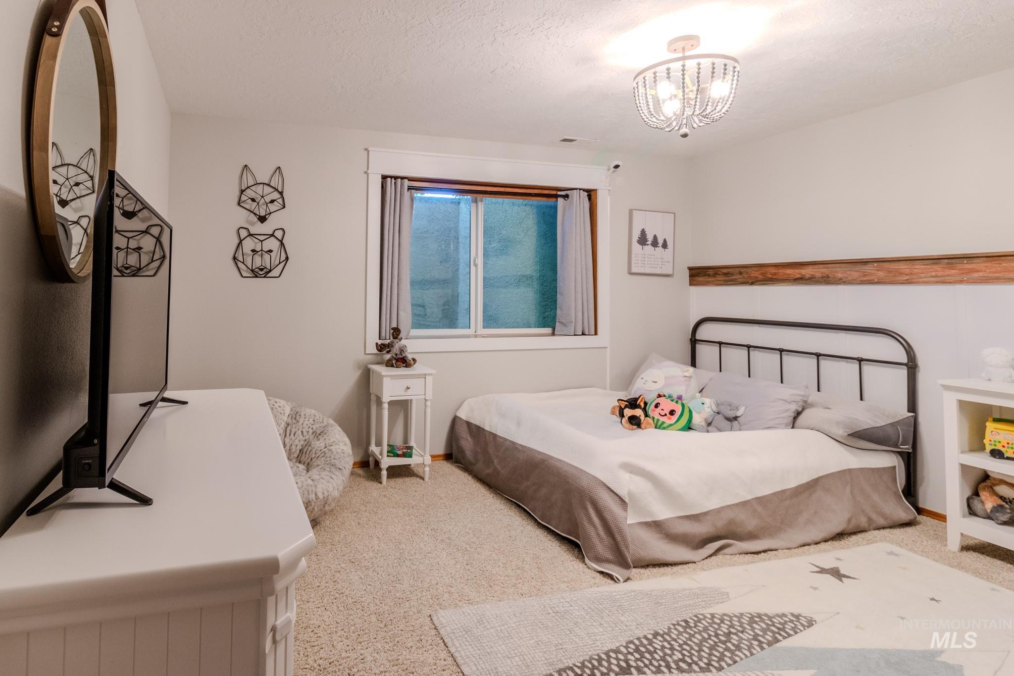 Carpeted bedroom featuring a chandelier and a textured ceiling