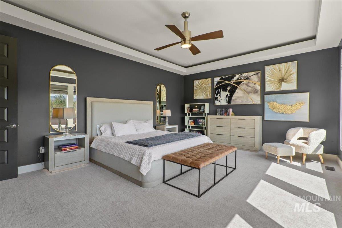 Carpeted bedroom with a tray ceiling, ceiling fan, and arched walkways