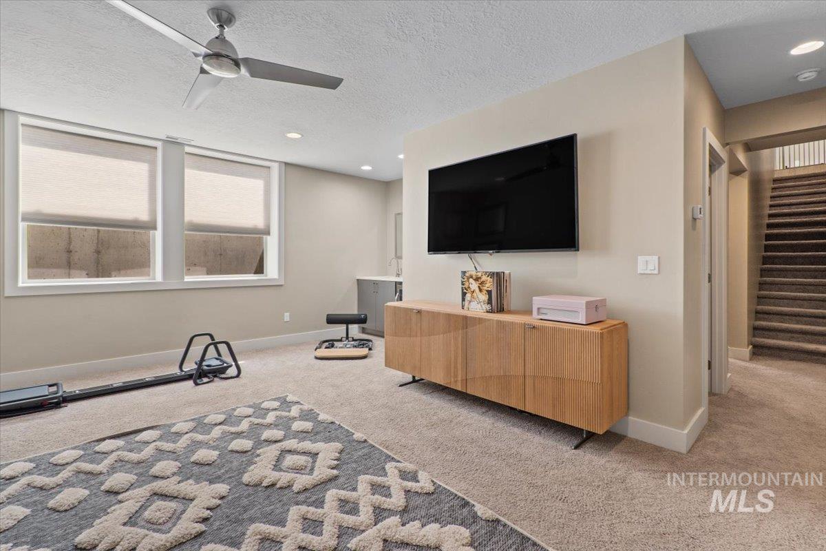 Living room with carpet flooring, ceiling fan, stairway, a textured ceiling, and recessed lighting
