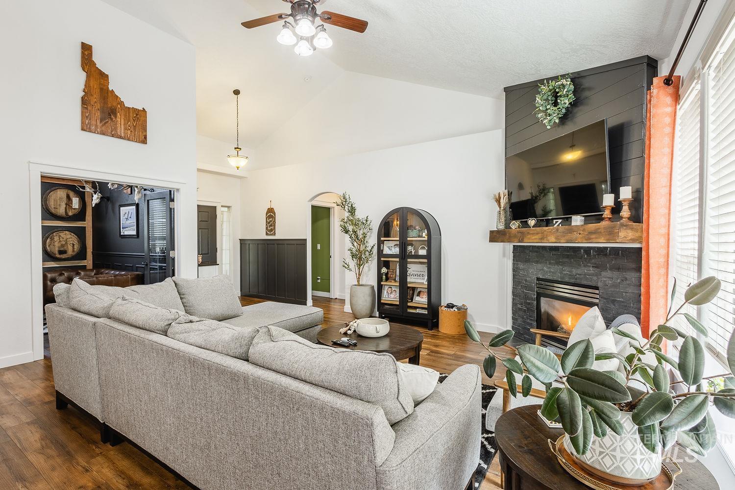 Living area with wood finished floors, a stone fireplace, ceiling fan, high vaulted ceiling, and healthy amount of natural light