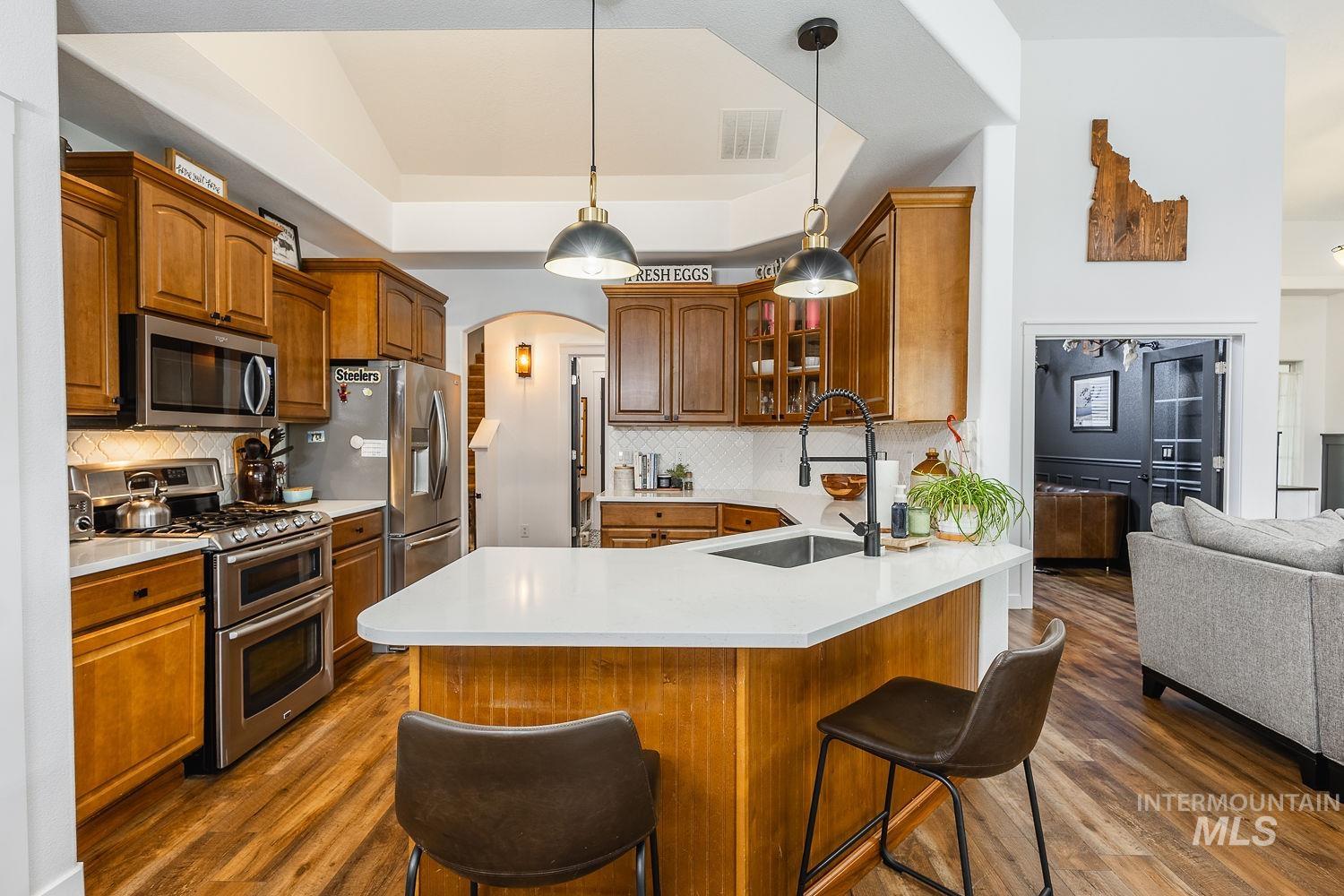 Kitchen featuring arched walkways, appliances with stainless steel finishes, tasteful backsplash, and dark wood-type flooring