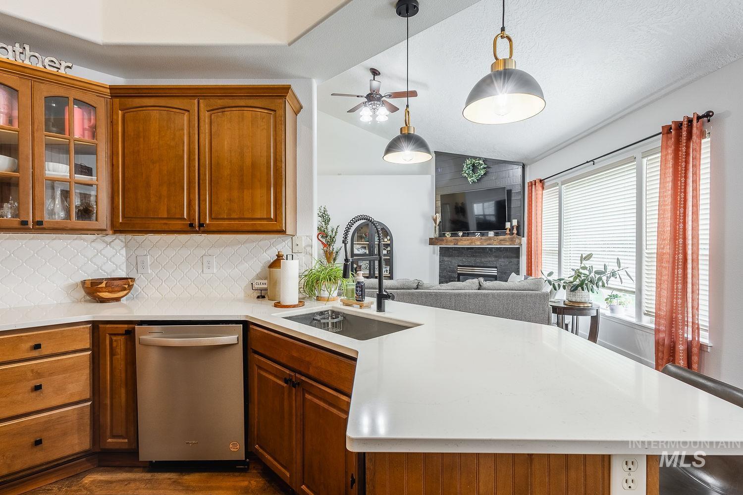 Kitchen featuring vaulted ceiling, a fireplace, dishwasher, glass insert cabinets, and light stone counters
