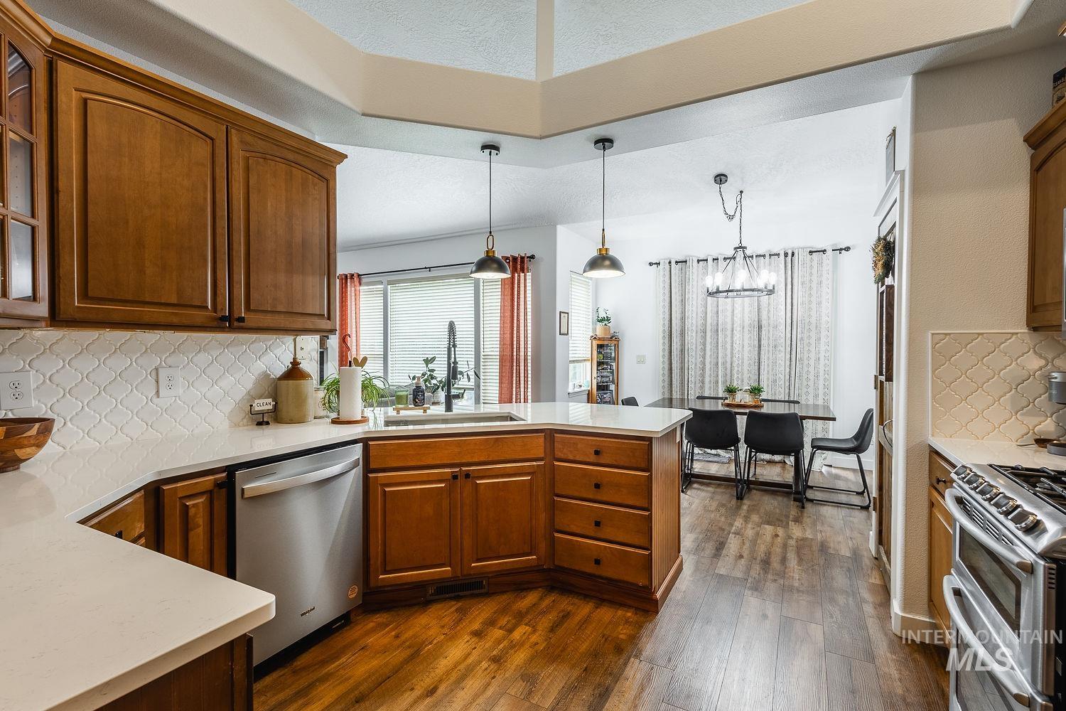 Kitchen with tasteful backsplash, a peninsula, stainless steel appliances, dark wood finished floors, and brown cabinets