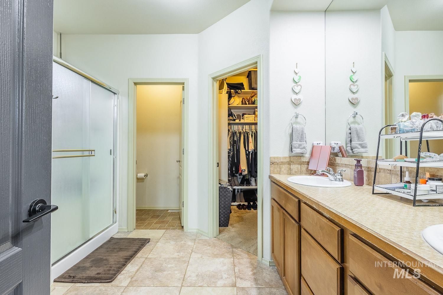 Full bath featuring double vanity, a spacious closet, a stall shower, and light tile patterned floors