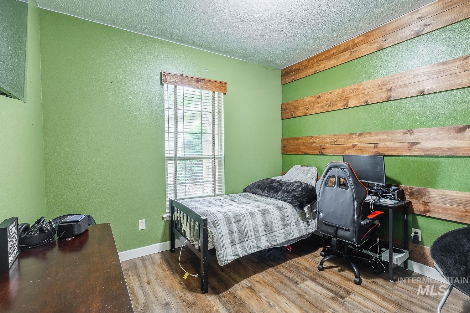 Bedroom featuring wood finished floors, a textured ceiling, a desk, and a textured wall