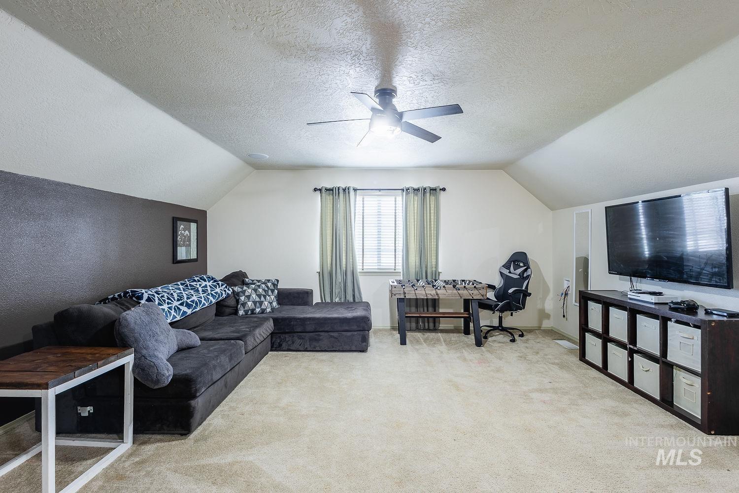 Home office with light colored carpet, vaulted ceiling, a textured ceiling, and ceiling fan