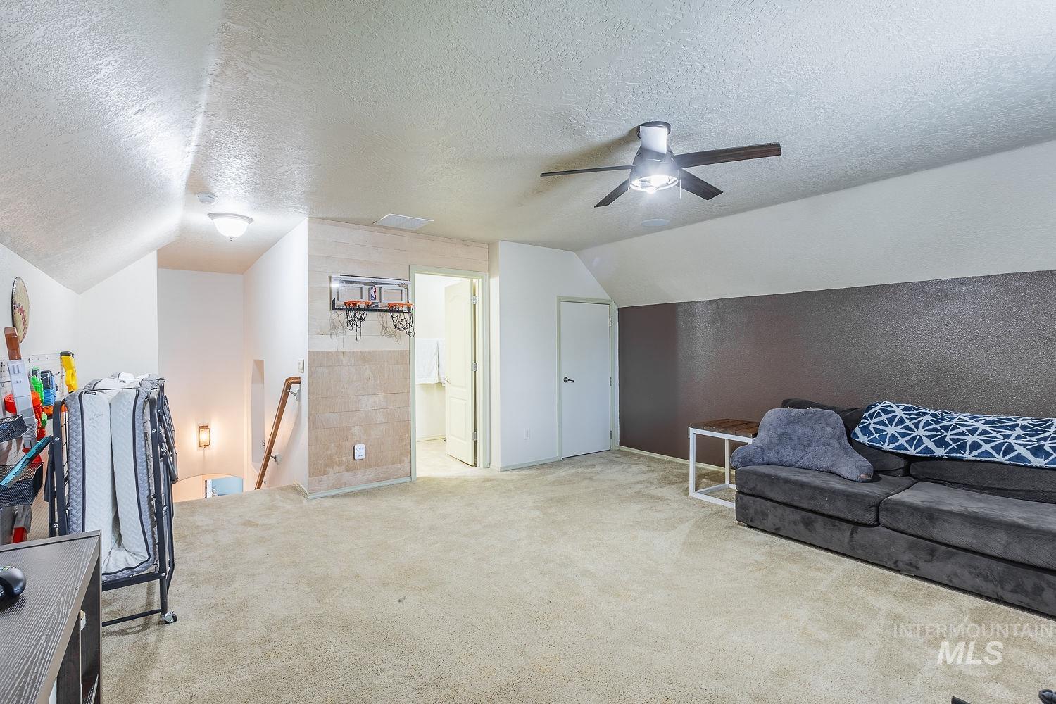 Sitting room with an upstairs landing, a textured ceiling, carpet flooring, lofted ceiling, and a ceiling fan