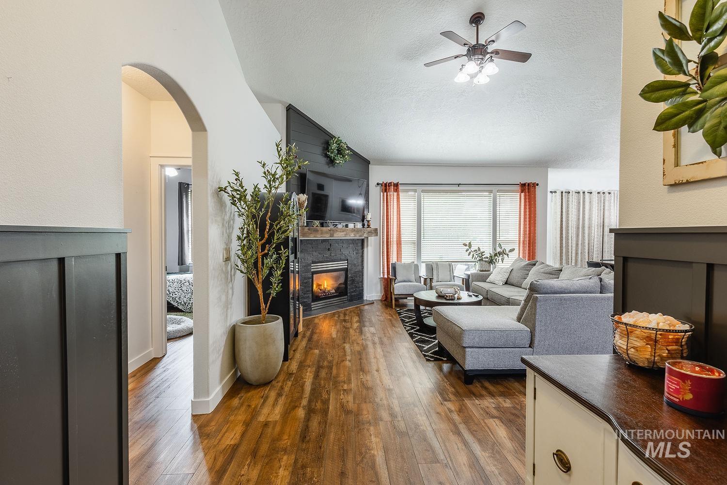 Living area featuring a glass covered fireplace, dark wood finished floors, a textured ceiling, arched walkways, and a ceiling fan