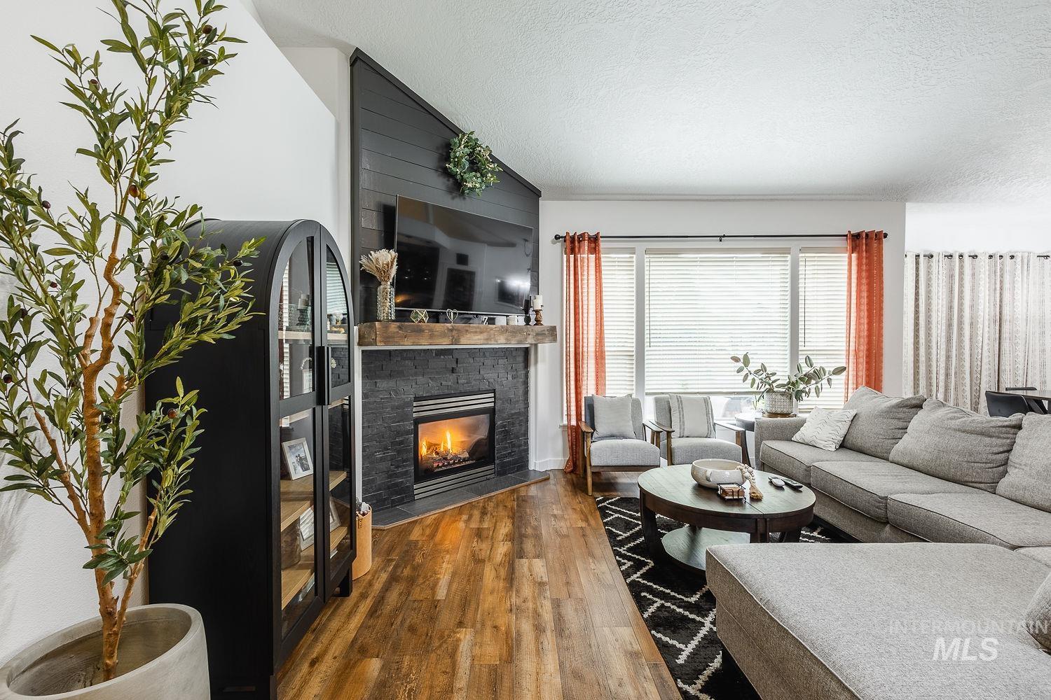 Living area with a textured ceiling, wood finished floors, a stone fireplace, and lofted ceiling