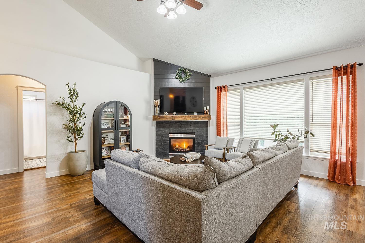 Living area featuring arched walkways, a glass covered fireplace, dark wood-type flooring, ceiling fan, and a textured ceiling