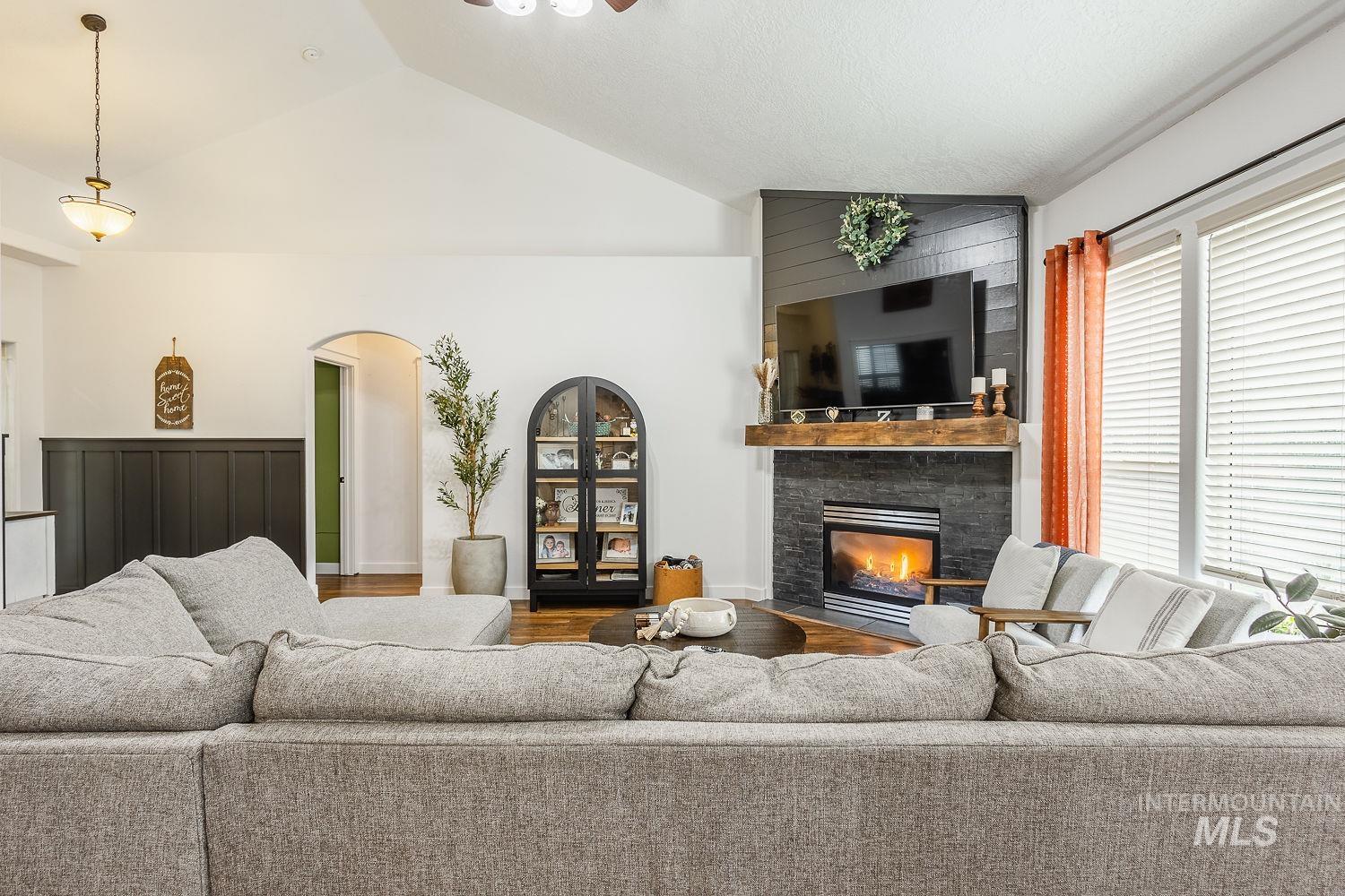 Living room with vaulted ceiling, a fireplace, a ceiling fan, arched walkways, and wood finished floors