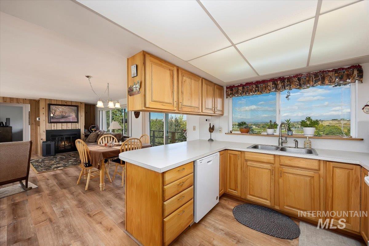 Kitchen with light countertops, white dishwasher, open floor plan, a peninsula, and light wood finished floors