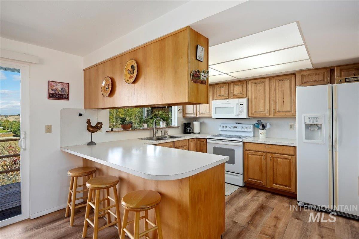 Kitchen featuring white appliances, a peninsula, a kitchen breakfast bar, light countertops, and light wood-style floors