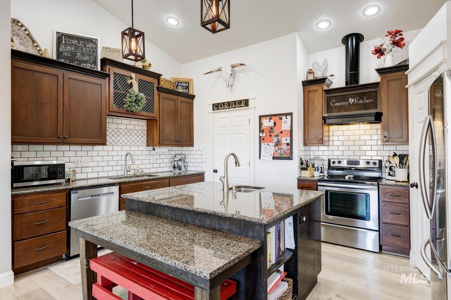 Kitchen with dark stone counters, appliances with stainless steel finishes, open shelves, a kitchen island with sink, and tasteful backsplash