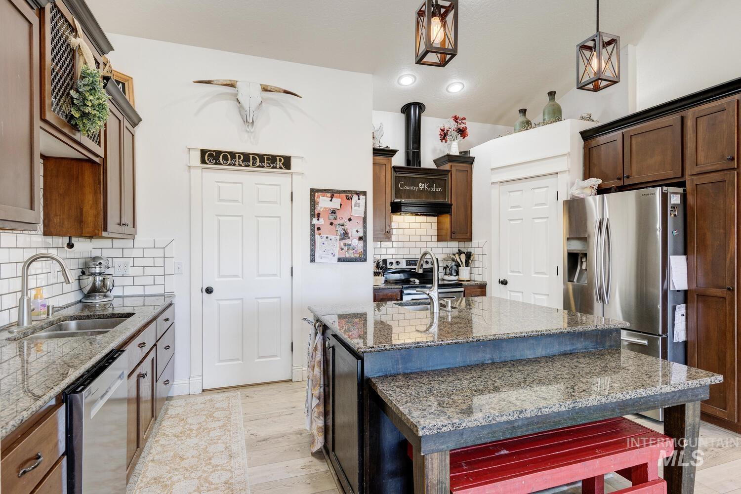 Kitchen featuring dark stone countertops, appliances with stainless steel finishes, tasteful backsplash, a center island with sink, and decorative light fixtures