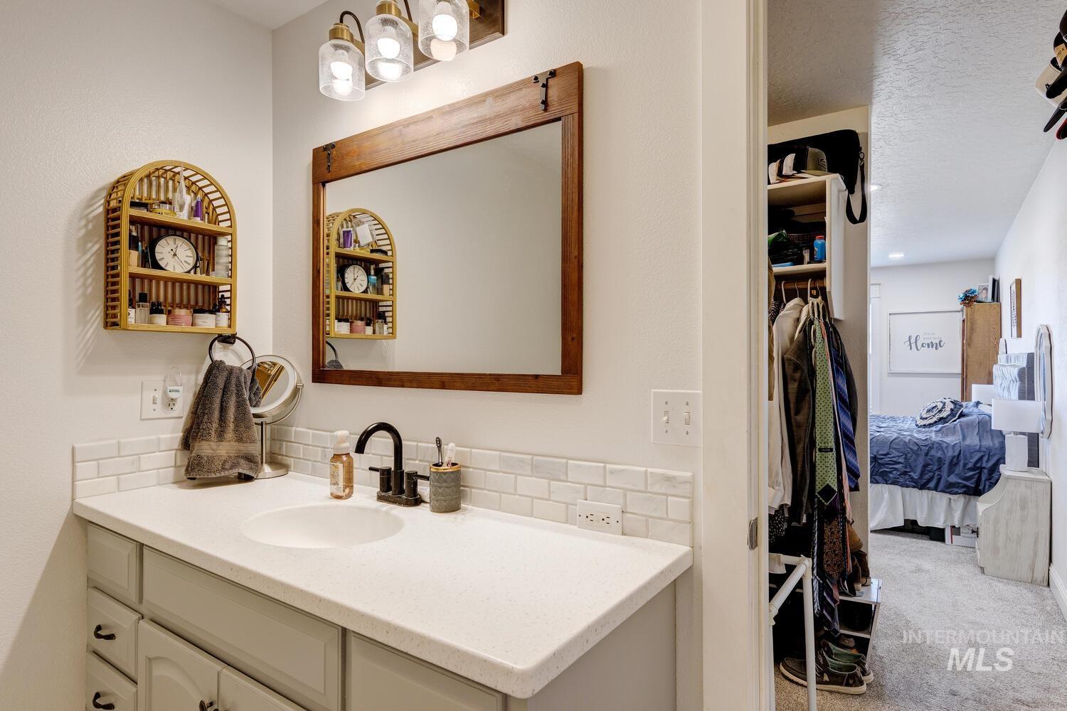 Bathroom featuring vanity, light carpet, decorative backsplash, a textured ceiling, and a walk in closet