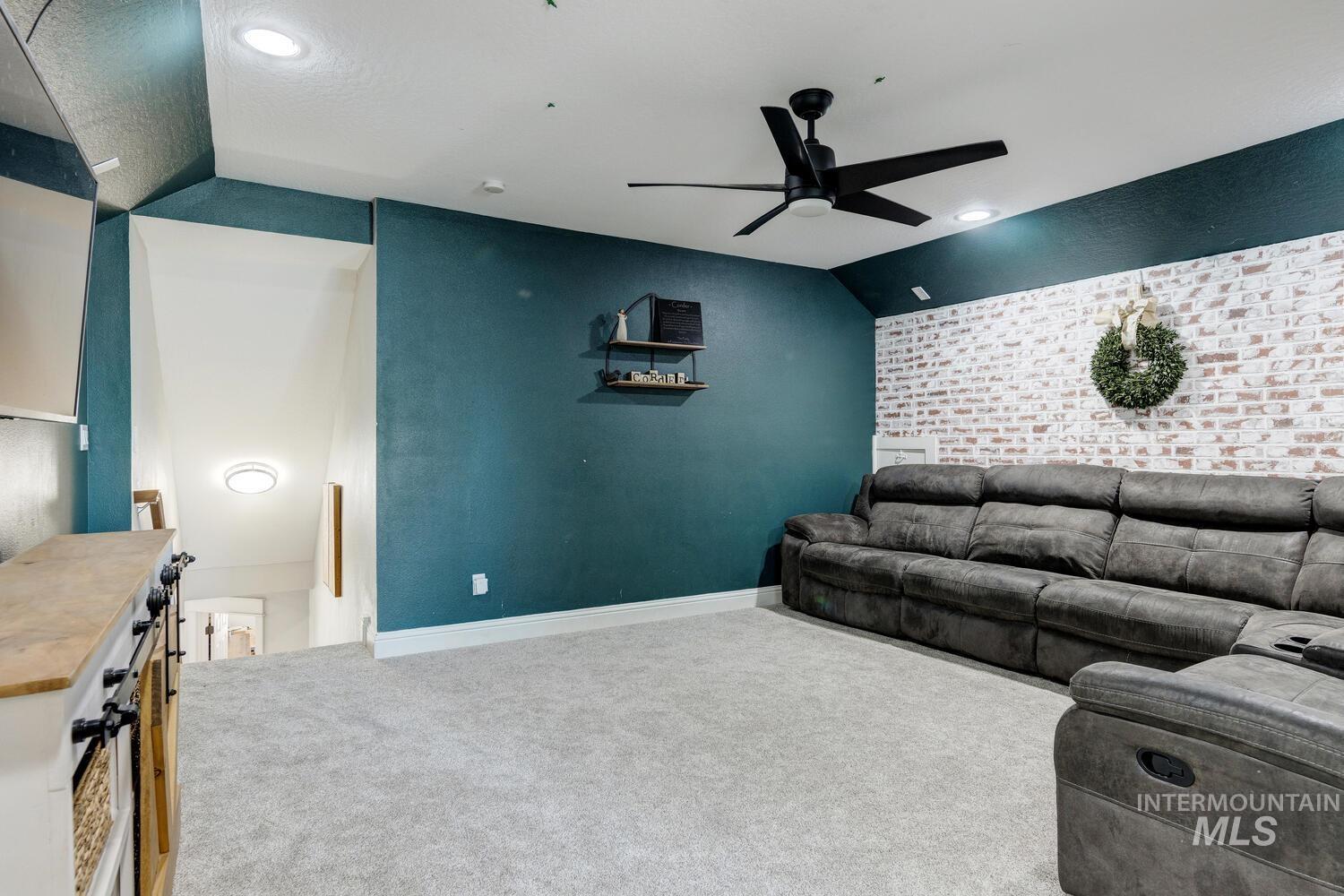 Living area featuring an accent wall, light carpet, ceiling fan, and vaulted ceiling