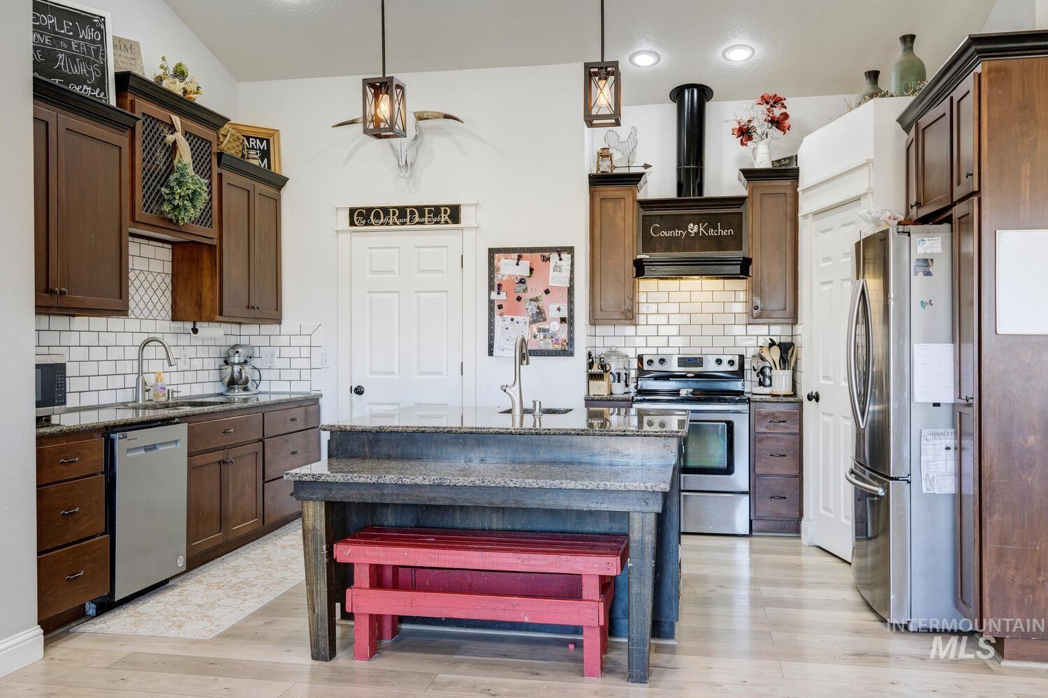 Kitchen with dark stone counters, appliances with stainless steel finishes, pendant lighting, and backsplash