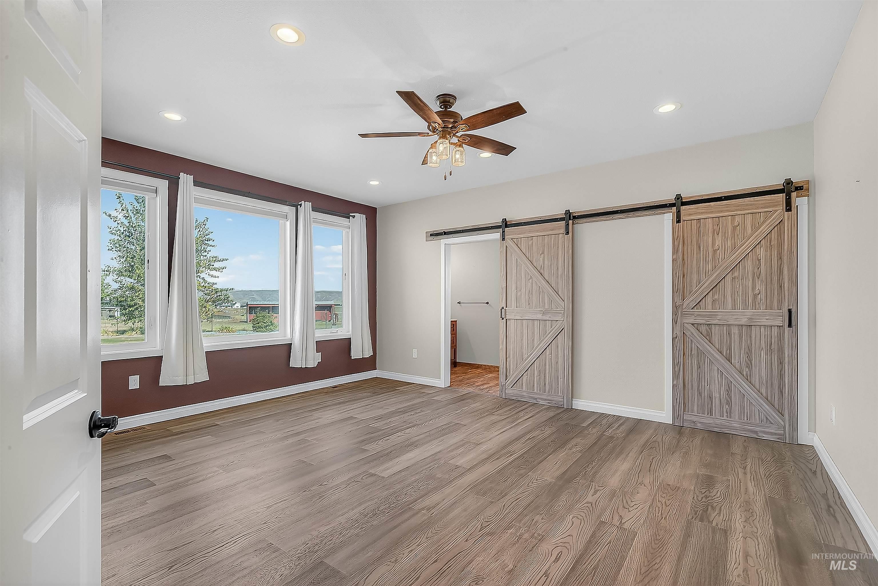 Unfurnished bedroom featuring ceiling fan, light wood-style flooring, recessed lighting, and a barn door